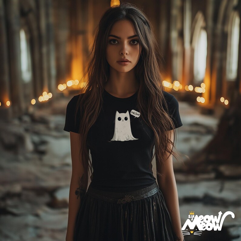 May include: A woman with long dark hair is wearing a black t-shirt with a white ghost cat graphic and the word "MEOW" in a speech bubble. She is also wearing a black skirt.