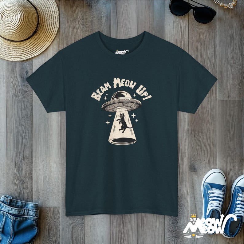 May include: A dark blue t-shirt with a graphic of a black cat being beamed up in a UFO. The text on the shirt reads "Beam Meow Up!"