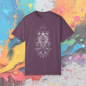 May include: A maroon t-shirt featuring a white graphic of a cat's face above a lotus flower. The cat design has geometric and floral elements. The shirt is a crew neck style.