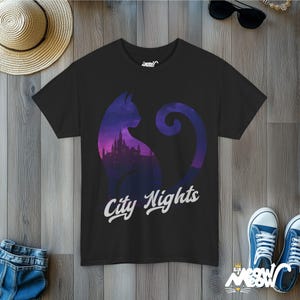 Young woman in a clothing store with colorful t-shirts behind her. She is wearing a black -t-shirt with the outline of a cat sitting.Inside the shape of the cat in a twilight city skyline in purple colors.