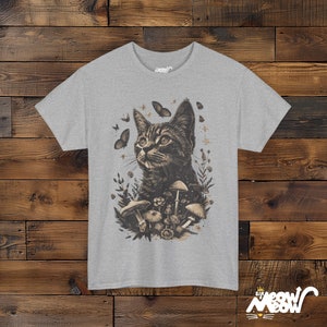 Vintage style t-shirt print of a cat in the woodlands surrounded by wildflowers, mushrooms and butterflies. Gray tee.