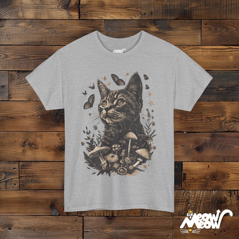 Vintage style t-shirt print of a cat in the woodlands surrounded by wildflowers, mushrooms and butterflies. Gray tee.