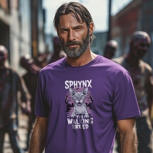 以下が含まれることがあります： 紫色のTシャツ。スフィンクス猫のグラフィックが特徴で、猫の上に「SPHYNX」、下に「THE WALKING BREED」の文字。猫のグラフィックは、木や墓石のある不気味な墓地のシーンを背景にしています。