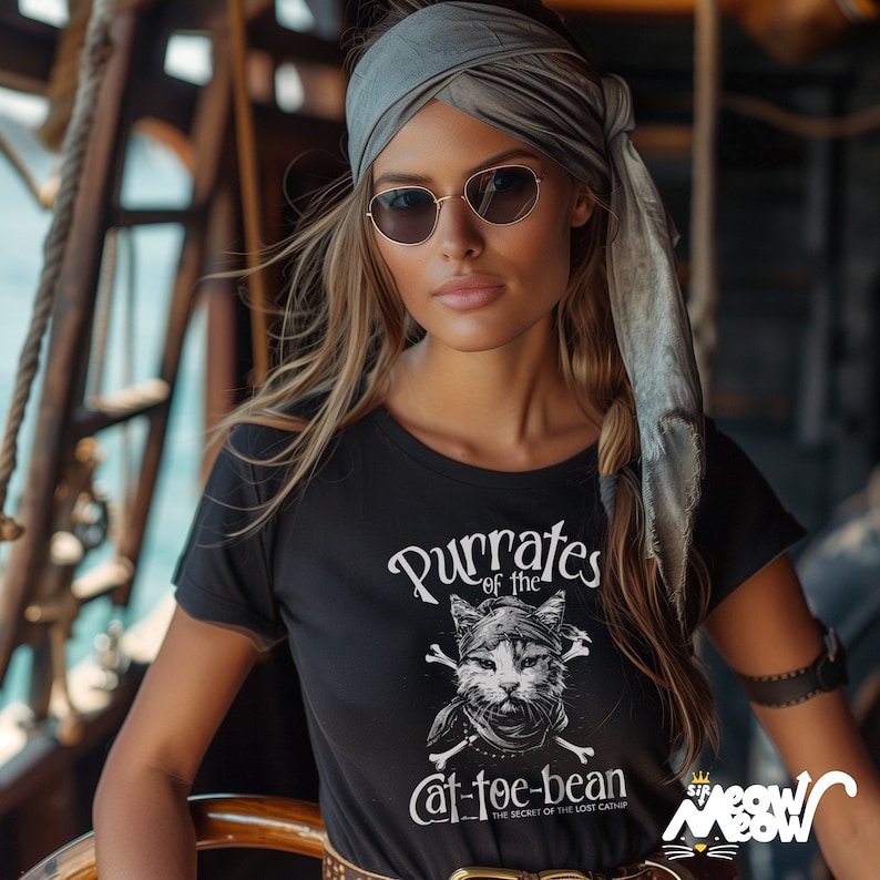 May include: A black t-shirt with a white graphic of a cat wearing a pirate bandana and holding crossed bones. The text on the shirt reads "Purrates of the Cat-toe-bean The Secret of the Lost Catnip".