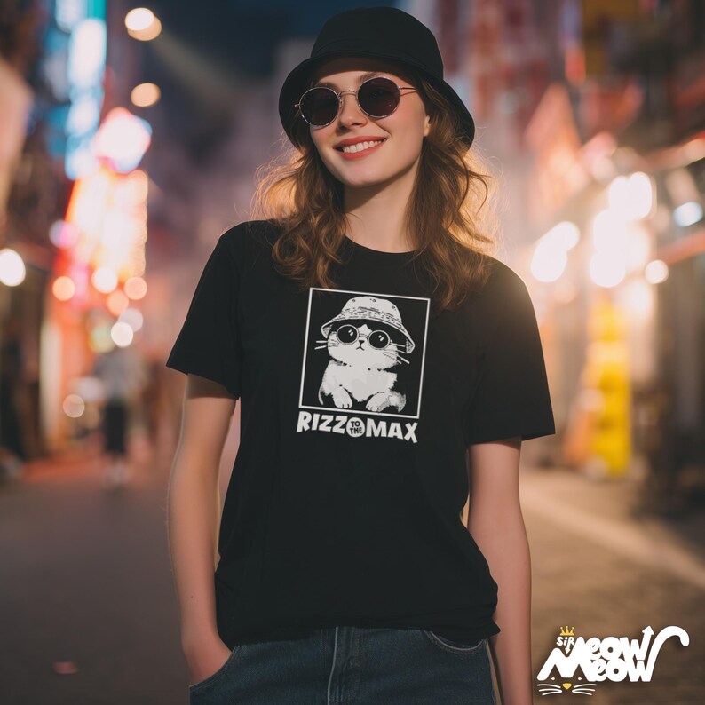 May include: Black t-shirt featuring a white graphic of a cat wearing sunglasses and a bucket hat, within a black square. The text "RIZZOMAX" is below the graphic. The shirt is short-sleeved.