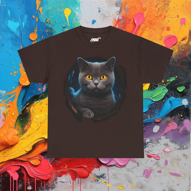 May include: A brown t-shirt with a graphic of a gray cat with yellow eyes peeking out of a hole. The cat is looking directly at the viewer.