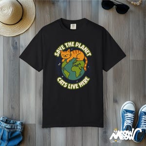 以下が含まれることがあります： 地球で眠る猫のグラフィックがプリントされた黒いTシャツ。テキストは「地球を救え 猫はここに住んでいる」です。