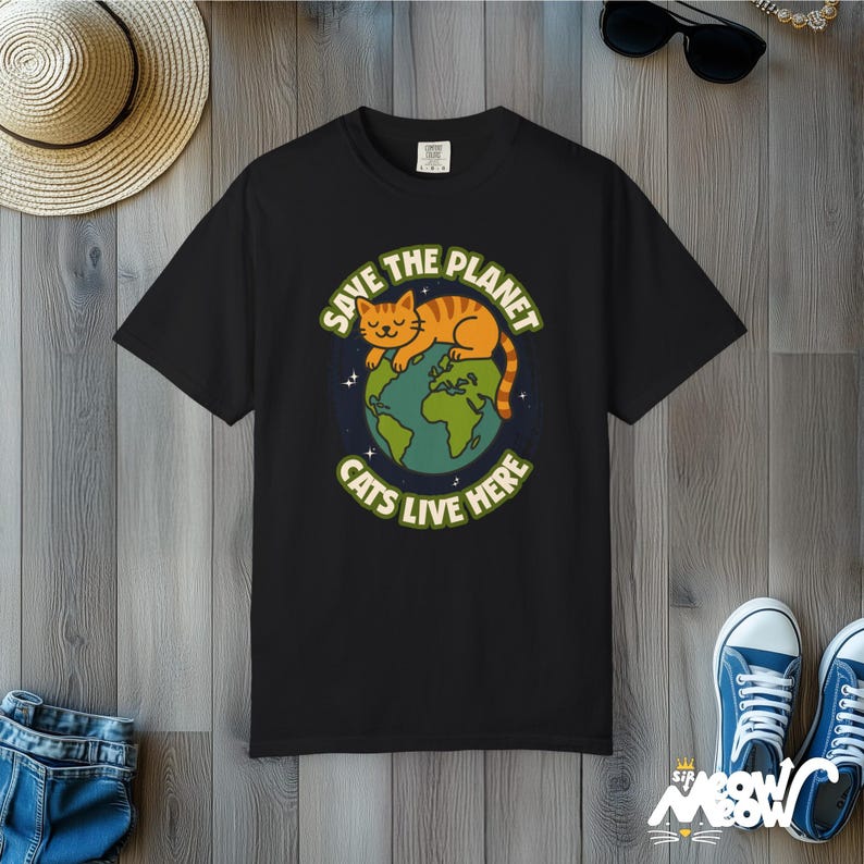 以下が含まれることがあります： 地球で眠る猫のグラフィックがプリントされた黒いTシャツ。テキストは「地球を救え 猫はここに住んでいる」です。