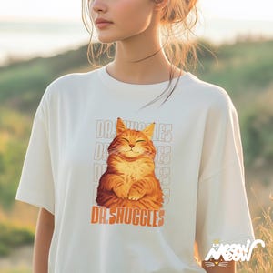 May include: A white t-shirt with a graphic of a smiling orange cat with the text "Dr. Snuggles" printed on the front.