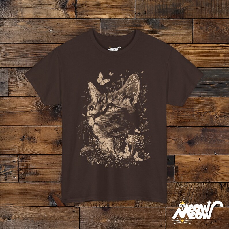 Vintage style t-shirt print of a cat in the woodlands surrounded by wildflowers, mushrooms and butterflies. Chocolate brown tee.