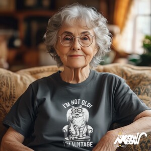 May include: A gray t-shirt with a graphic of a cat wearing glasses and sitting in a chair. The text on the shirt reads "I'm not old! I'm vintage."