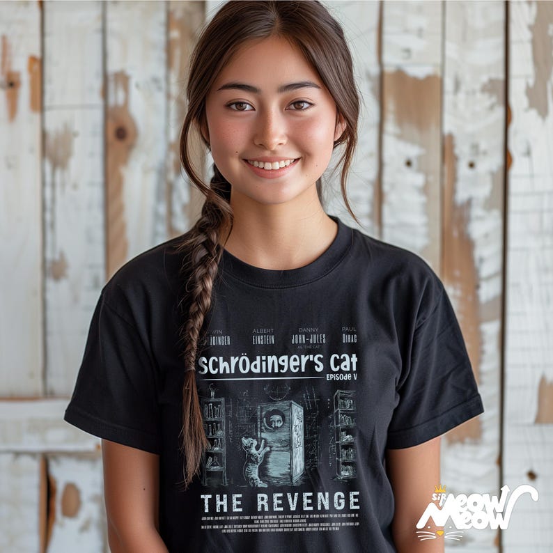 May include: A woman wearing a black t-shirt with a graphic of a cat in a box. The graphic is a parody of the movie poster for "Schr&ouml;dinger's Cat: The Revenge".