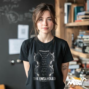 May include: Black t-shirt with a graphic featuring four cat portraits and the text "THE ENTANGLED TWO CATS, ONE FATE." The design includes scientific diagrams. The shirt has a crew neck and short sleeves.