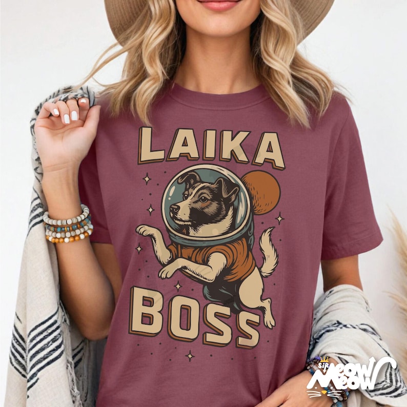 K&ouml;nnte beinhalten: Burgunderfarbenes T-Shirt mit einem Retro-Design, das einen Hund mit Weltraumhelm zeigt. Der Text lautet "LAIKA BOSS". Die Hundeillustration tr&auml;gt einen braunen Raumanzug. Das Design beinhaltet Sterne und eine Sonne.