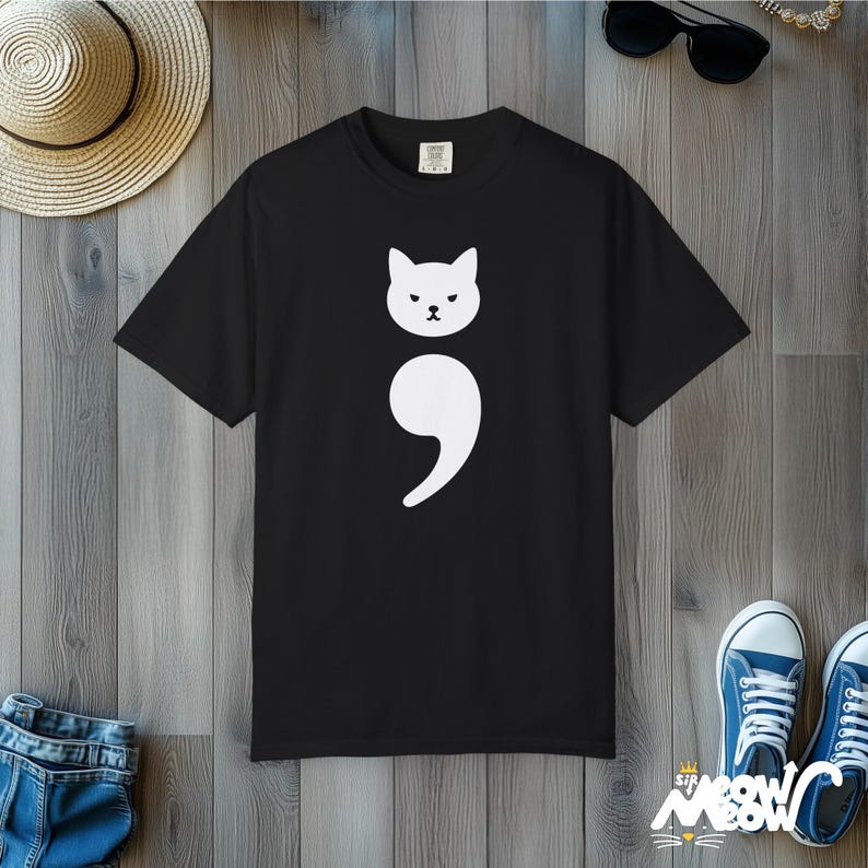 May include: Black t-shirt with a white graphic of a cat with a semicolon above it.