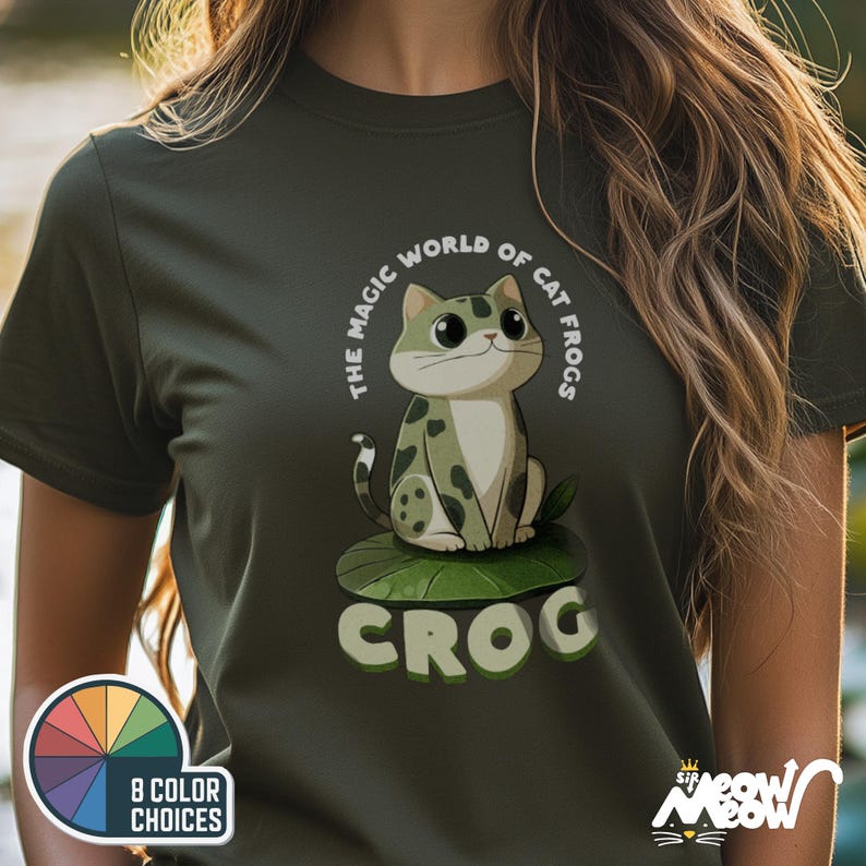 May include: A dark green t-shirt with a cartoon cat wearing a green frog costume. The text on the shirt reads "The Magic World of Cat Frogs, Croc".