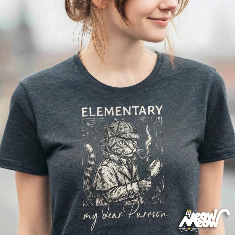 May include: Dark gray t-shirt featuring a cartoon cat dressed as Sherlock Holmes, complete with a hat, coat, pipe, and magnifying glass. The text "ELEMENTARY my dear Purrson" is printed above and below the illustration. The Sir Meow logo is in the bottom right.