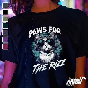 K&ouml;nnte beinhalten: Schwarzes T-Shirt mit einem Grafikdruck eines Katzen mit Sonnenbrille und Kopfh&ouml;rern. Der Text "PAWS FOR THE RIZZ" ist auf dem Shirt aufgedruckt.