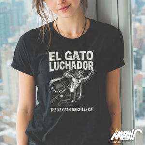 May include: Black t-shirt with the text "EL GATO LUCHADOR" above an illustration of a cat wrestler wearing a mask and cape. Below the illustration is the text "THE MEXICAN WRESTLER CAT".