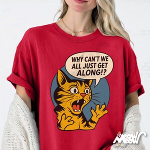 May include: Red t-shirt featuring a distressed graphic of a surprised orange cat with the text "WHY CAN'T WE ALL JUST GET ALONG!?" in a speech bubble. The cat is set against a blue circle.