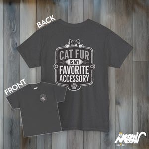 May include: A dark heather grey t-shirt with a vintage-style graphic that says "Cat fur is my favorite accessory". The graphic features a black cat peeking over the top of the text.
