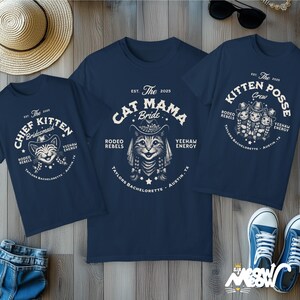May include: Navy blue t-shirts with white graphic designs. One shirt says "Chief Kitten Bridesmaid", another says "Cat Mama Bride", and the third says "Kitten Posse Crew". All shirts have a cat wearing a cowboy hat and the text "Rodeo Rebels".