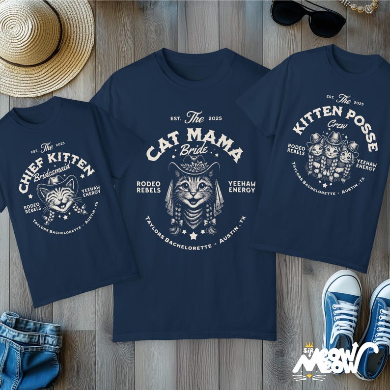 May include: Navy blue t-shirts with white graphic designs. One shirt says "Chief Kitten Bridesmaid", another says "Cat Mama Bride", and the third says "Kitten Posse Crew". All shirts have a cat wearing a cowboy hat and the text "Rodeo Rebels".