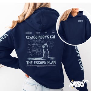 May include: A navy blue hoodie with a white graphic of a cat looking up at a chalkboard with equations and the text "Schrödinger's cat The Escape Plan".