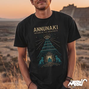 May include: Black t-shirt featuring the text "ANNUNAKI RETURN OF THE ARCHITECTS" above a teal and gold graphic of a pyramid with an eye and two cat-like figures. The design has a geometric and ancient theme.