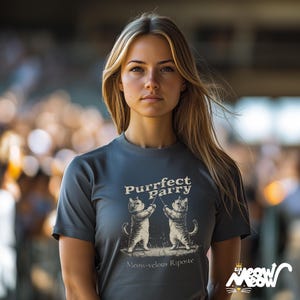 May include: A gray t-shirt with a graphic of two cats fencing. The text on the shirt reads "Purrfect Parry" and "Meow-velous Riposte".