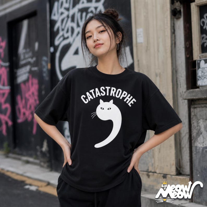 May include: Black t-shirt with the word "CATASTROPHE" above a white cat-shaped design. The cat's tail forms a number nine. The shirt also has the text "sip meow meow" with a cat face logo.