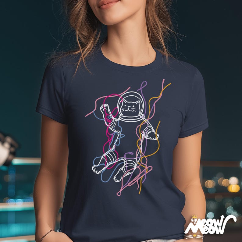 May include: Navy blue t-shirt featuring a white outline illustration of a cat in an astronaut suit, with colorful lines. The shirt has the text "Sir Meow Meow" at the bottom right.
