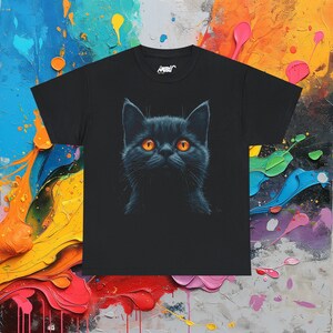 May include: Black t-shirt featuring a detailed illustration of a black cat with bright orange eyes. The cat's face is centered on the shirt, creating a striking contrast against the dark fabric. The shirt has a crew neck and short sleeves.