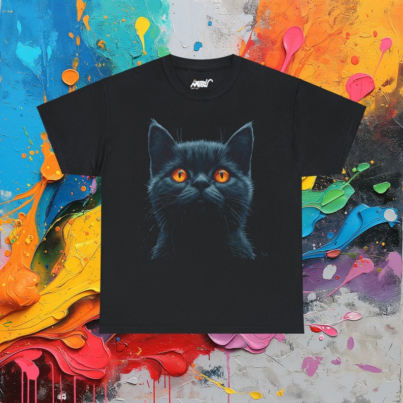 May include: Black t-shirt featuring a detailed illustration of a black cat with bright orange eyes. The cat's face is centered on the shirt, creating a striking contrast against the dark fabric. The shirt has a crew neck and short sleeves.