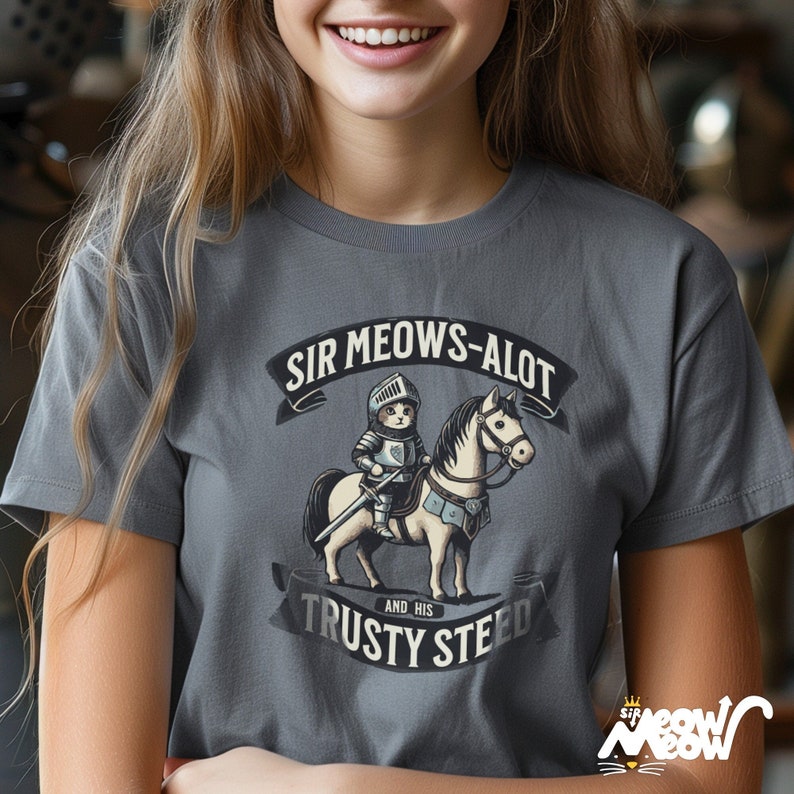 May include: A gray t-shirt with a cartoon illustration of a cat in knight armor riding a horse. The text "Sir Meows-Alot and His Trusty Steed" is printed on the shirt.