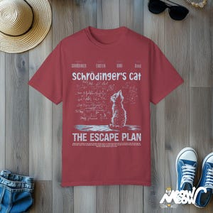 May include: A red t-shirt with a white graphic of a cat looking up at a chalkboard with equations and the text "Schr&ouml;dinger's Cat The Escape Plan".