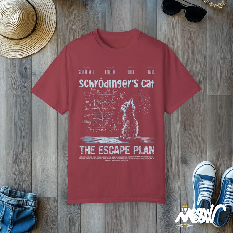 May include: A red t-shirt with a white graphic of a cat looking up at a chalkboard with equations and the text "Schr&ouml;dinger's Cat The Escape Plan".