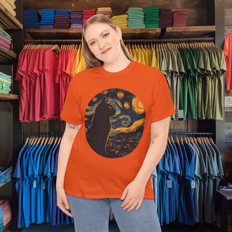 Peut inclure: Une femme portant un t-shirt orange avec une silhouette de chat noir devant un ciel &eacute;toil&eacute; de nuit. Le design est une reconstitution du c&eacute;l&egrave;bre tableau de Vincent van Gogh, "La Nuit &eacute;toil&eacute;e."
