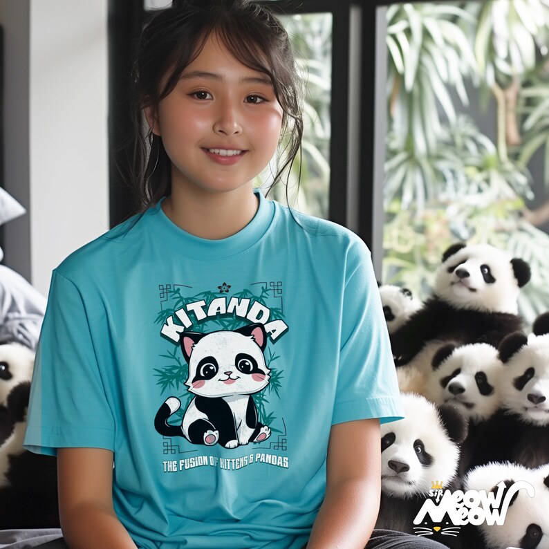 May include: A young person wearing a turquoise blue t-shirt with a panda graphic. The graphic features a black and white panda with the text "Kitanda The Fusion of Kittens & Pandas".