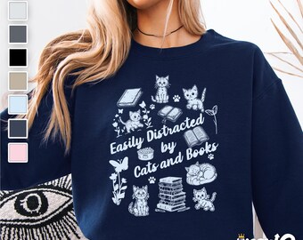 May include: A navy blue sweatshirt with a white graphic design featuring cats, books, and the text "Easily Distracted by Cats and Books".
