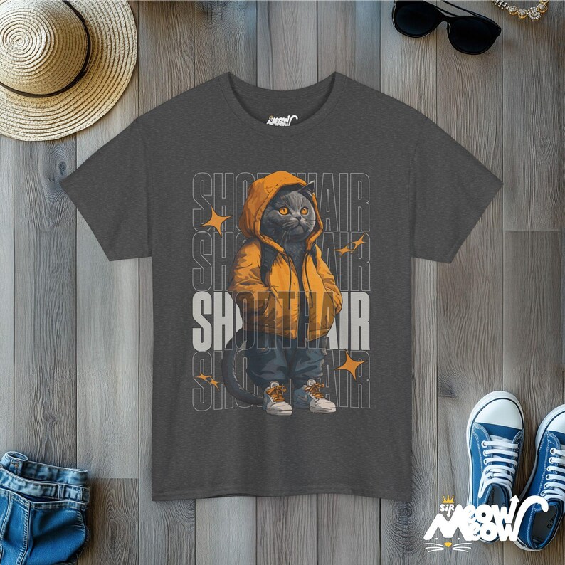 Humanized British Shorthair Cat standing up wearing a yellow hoodie and white and gray sneakers. Behind the cat is a stack of the word "Shorthair". The design appears on a woman wearing a dark heather tee.