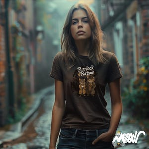 Puede incluir: Una camiseta marr&oacute;n con un gr&aacute;fico de dos gatos con sombreros y el texto "Purrlock & Ratson".