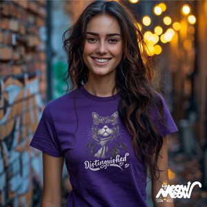 May include: Purple t-shirt featuring a graphic of a cat wearing sunglasses and a scarf. The text "Distinguished" is printed below the cat.