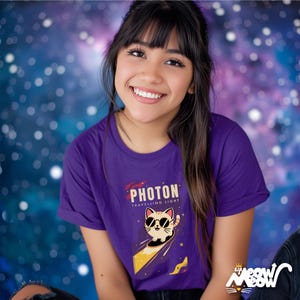 May include: A purple t-shirt featuring a graphic of a cat wearing sunglasses and riding a comet. The text "PHOTON TRAVELLING LIGHT" is printed on the shirt.