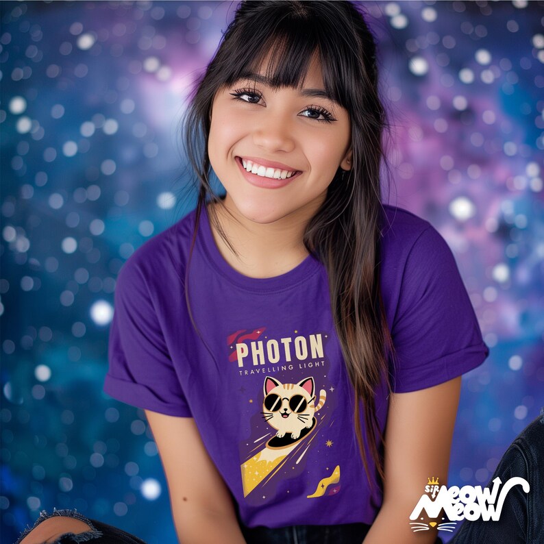 May include: A purple t-shirt featuring a graphic of a cat wearing sunglasses and riding a comet. The text "PHOTON TRAVELLING LIGHT" is printed on the shirt.