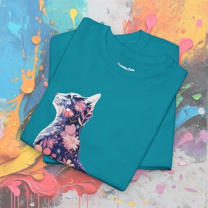 May include: Two teal t-shirts are stacked, each featuring a floral cat design. The cat's silhouette is filled with pink, purple, and white flowers. The shirts are made of a soft material and are suitable for casual wear.