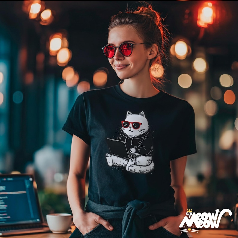 May include: Black t-shirt featuring a white cat wearing sunglasses and using a laptop. The cat is drawn in a cartoon style. The shirt is worn by a person with red sunglasses.