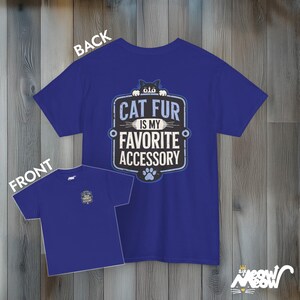 May include: A royal blue t-shirt with a black cat peeking over the top of a sign that reads "Cat Fur is my Favorite Accessory". The sign is in a vintage style with a blue paw print below it.