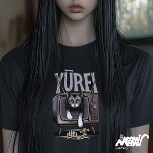 Op de afbeelding: Zwart T-shirt met een afbeelding van een kat in een vintage televisie. De tekst "YUREK" staat boven de televisie en de tekst "幽霊" staat onder de televisie.