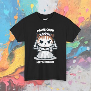 May include: Black t-shirt with a cartoon illustration of a cat wearing a white wedding dress and a flower crown. The text "PAWS OFF!! HE'S MINE!!" is printed below the cat.